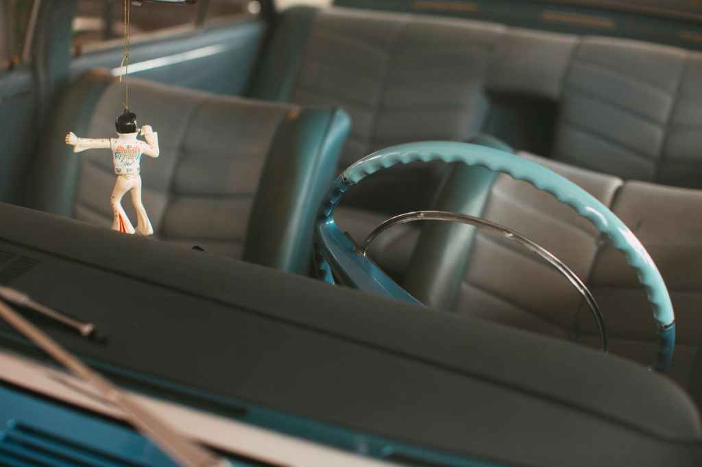 Elvis figurine hanging above dashboard showing interior of vintage car.